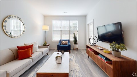 A living room with a white couch, a blue chair, a wooden coffee table, and a flat-screen TV mounted on the wall.