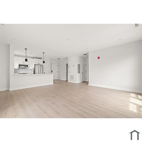 A spacious, empty room with wooden flooring and white walls.