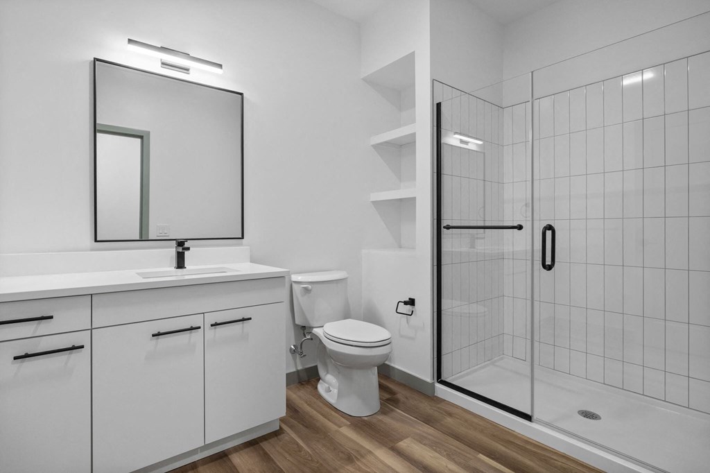 A white bathroom with a toilet, sink, mirror, and shelves.