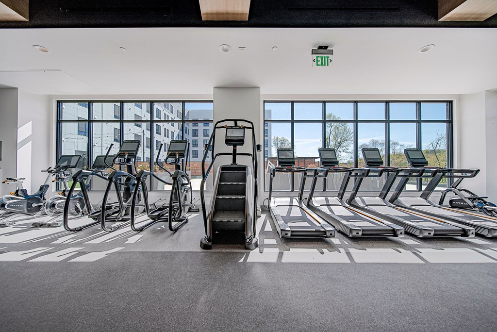 A gym with treadmills, exercise bikes and a green exit sign.