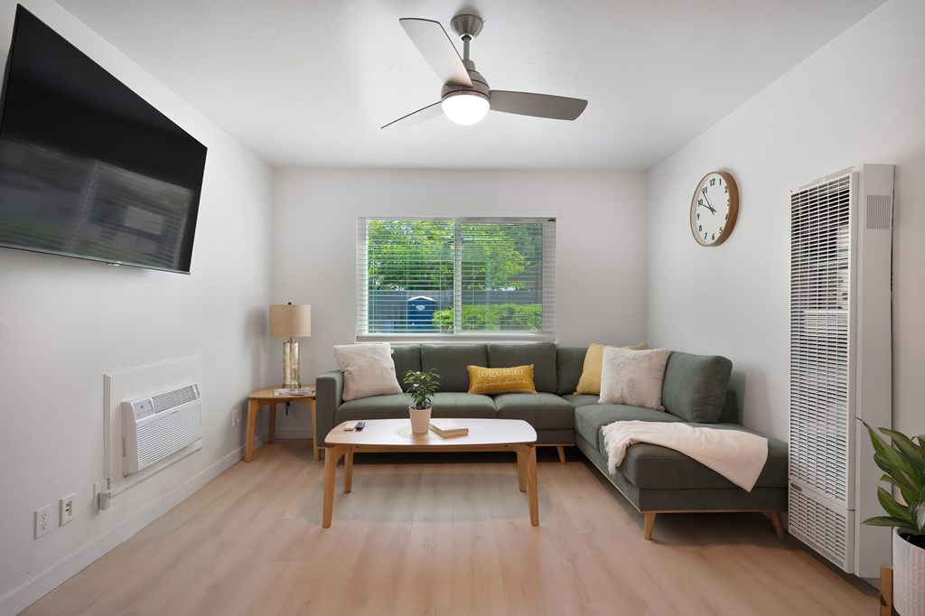 A living room with a grey couch, a wooden table, and a ceiling fan.