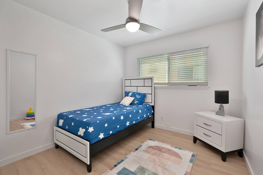 A bedroom with a bed, nightstand, and a rug on the floor.