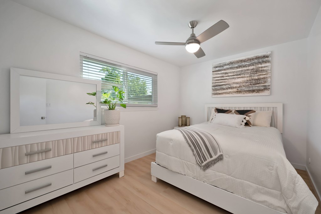 A white bedroom with a bed, dresser, and mirror.
