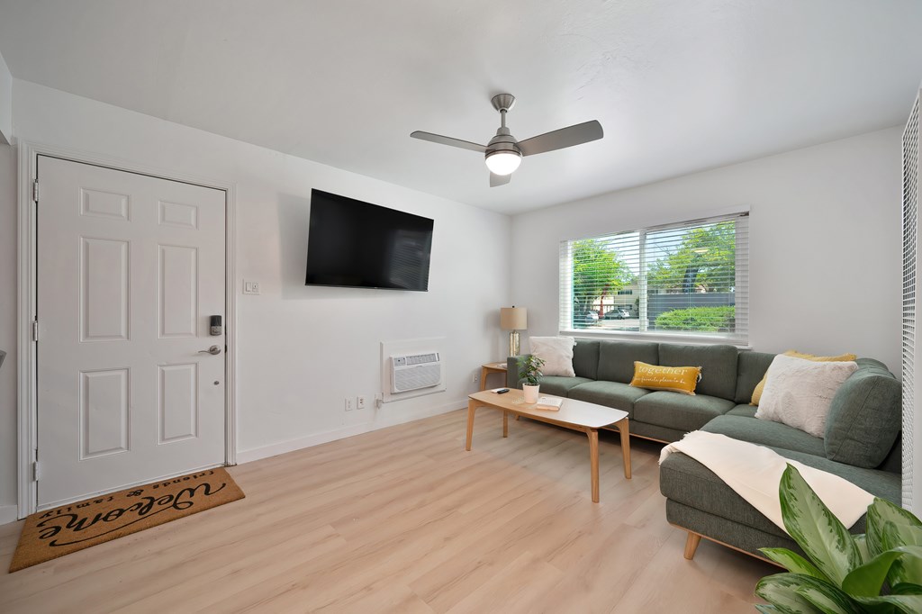 A living room with a couch, a coffee table, and a flat screen TV mounted on the wall.