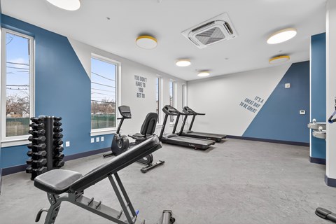 A gym with a row of treadmills and a weight rack.