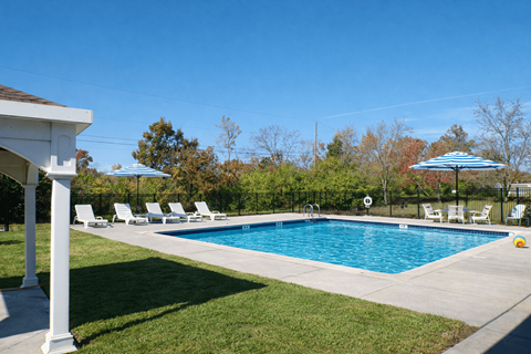A pool surrounded by lawn chairs and trees.