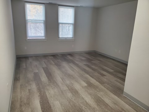 A room with wooden flooring and two windows.