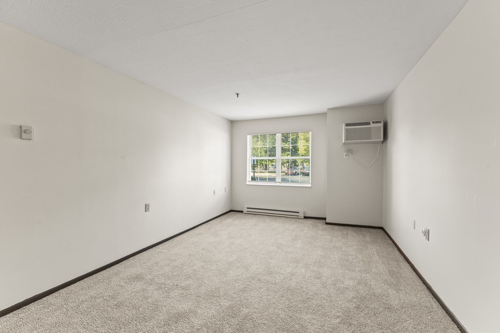 A sparsely furnished room with a window and a wall-mounted air conditioner.