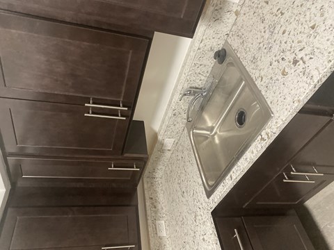A modern kitchen with a stainless steel sink and dark brown cabinets.
