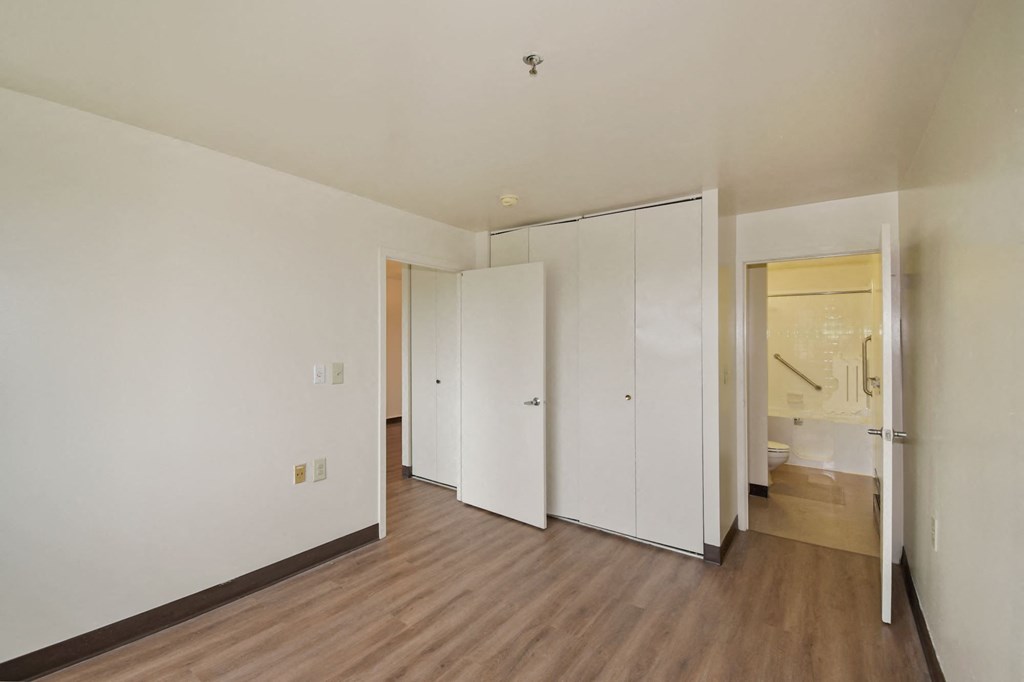 a bedroom with white walls and wood floors and a closet