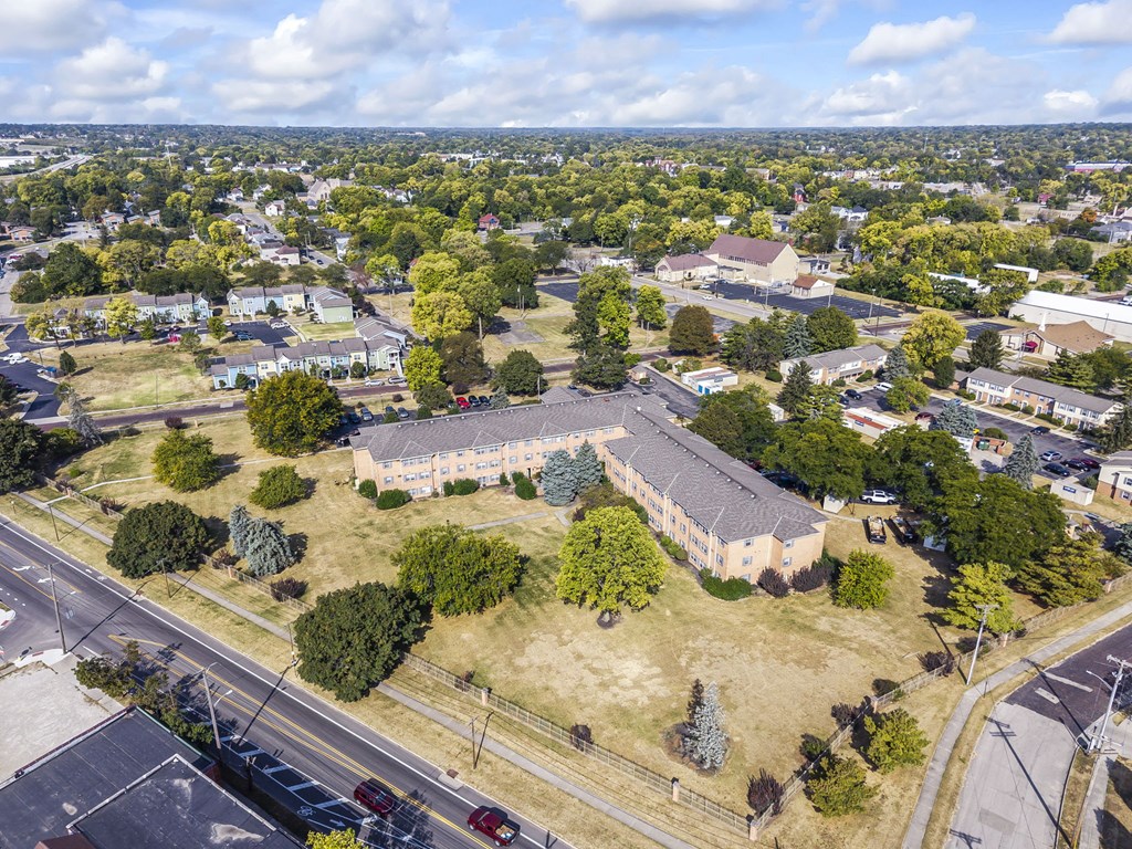 A large building with a grey roof is surrounded by trees and other buildings.