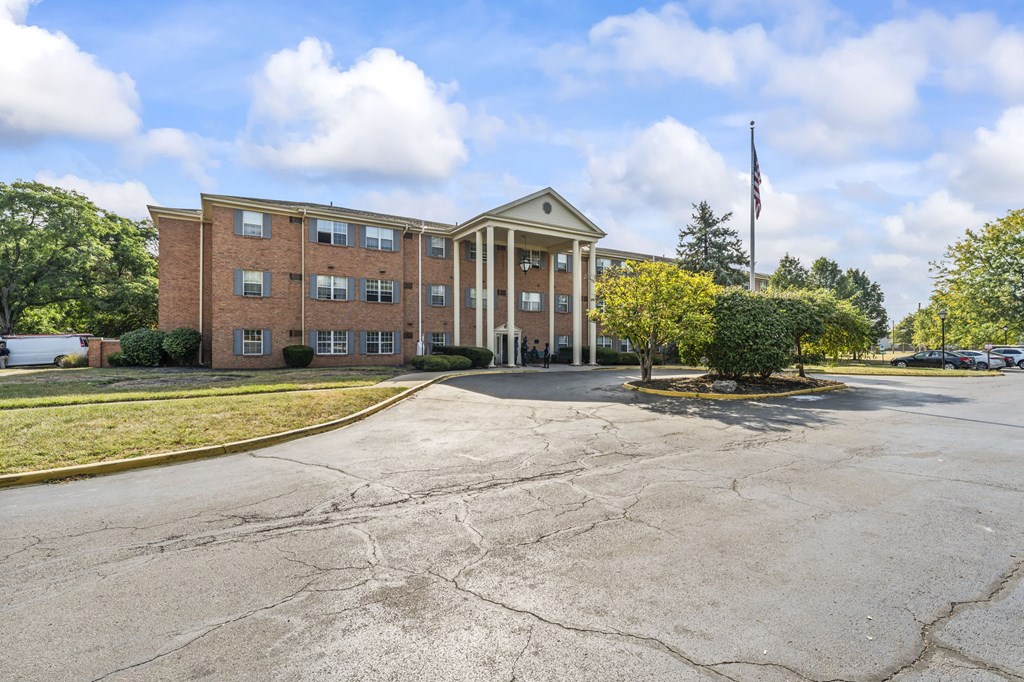 A large brick building with a flag on top stands in front of a parking lot.