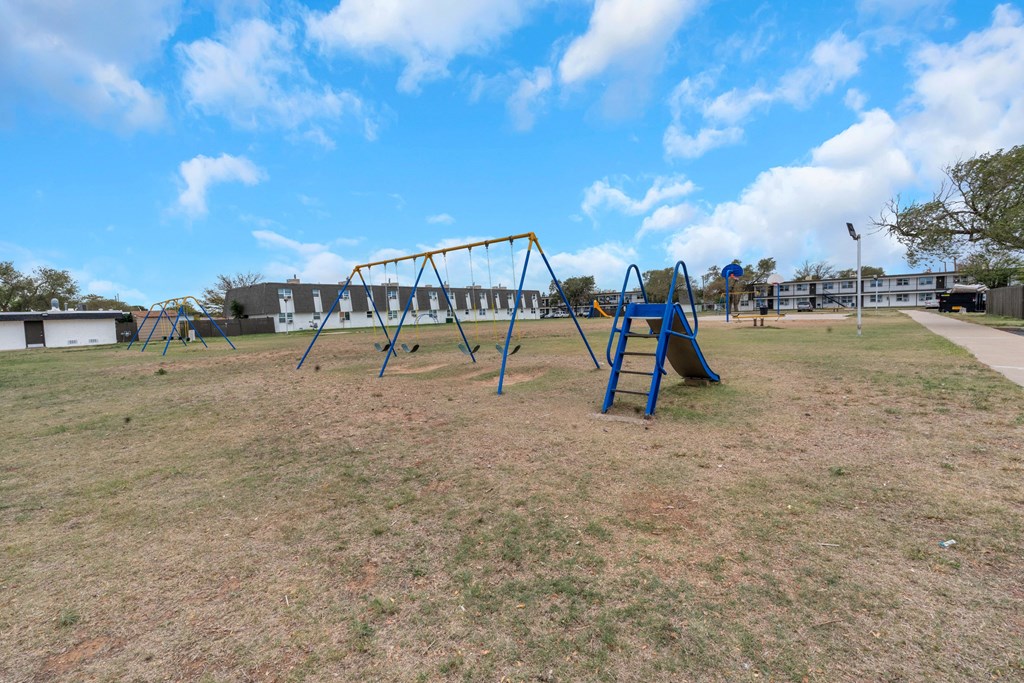 A playground with a blue swing set in the foreground.