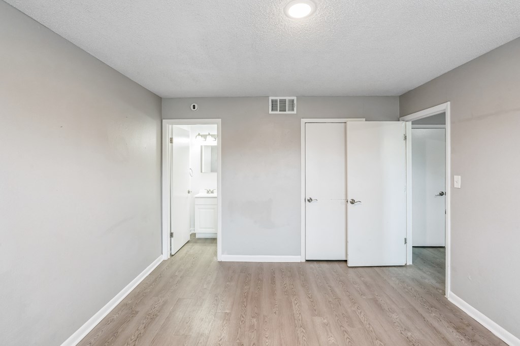 A room with white walls and wood flooring, featuring a white door and a white cabinet.