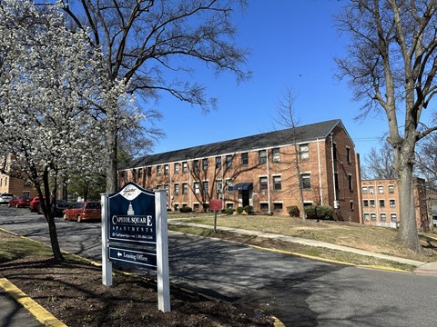 A sign for Cottage Square Apartments is in front of a brick building.