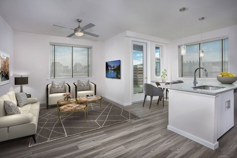 A modern living room with a white couch, a coffee table, and a kitchen area with a sink and a counter.