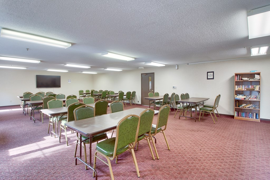 A room with tables and chairs and a television on the wall.