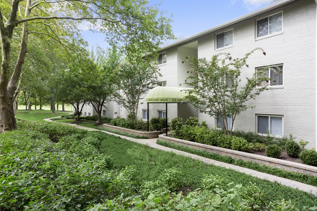 A white building with a green awning is surrounded by trees and bushes.