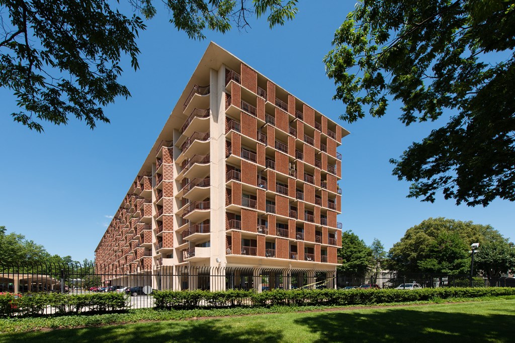 A tall red brick building with a triangular top is surrounded by trees and greenery.