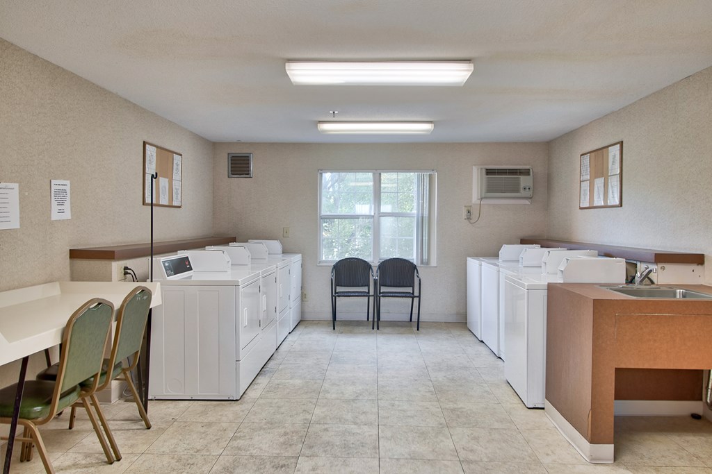 A room with a white table, chairs, and a sink.