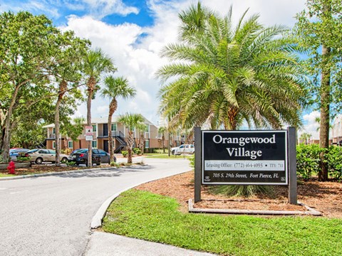 A sign for Orangewood Village stands in front of a row of palm trees.