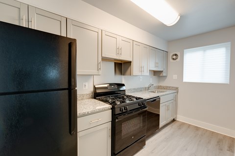 A black refrigerator sits in a kitchen with white cabinets.