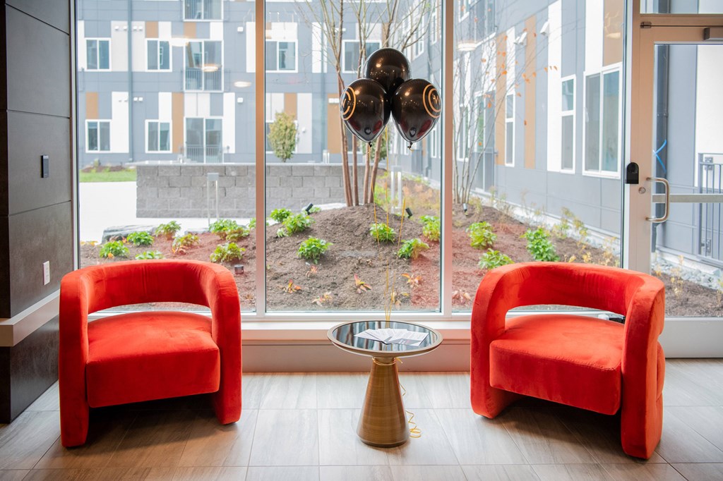 Two red chairs and a table in front of a window with a view of a garden.