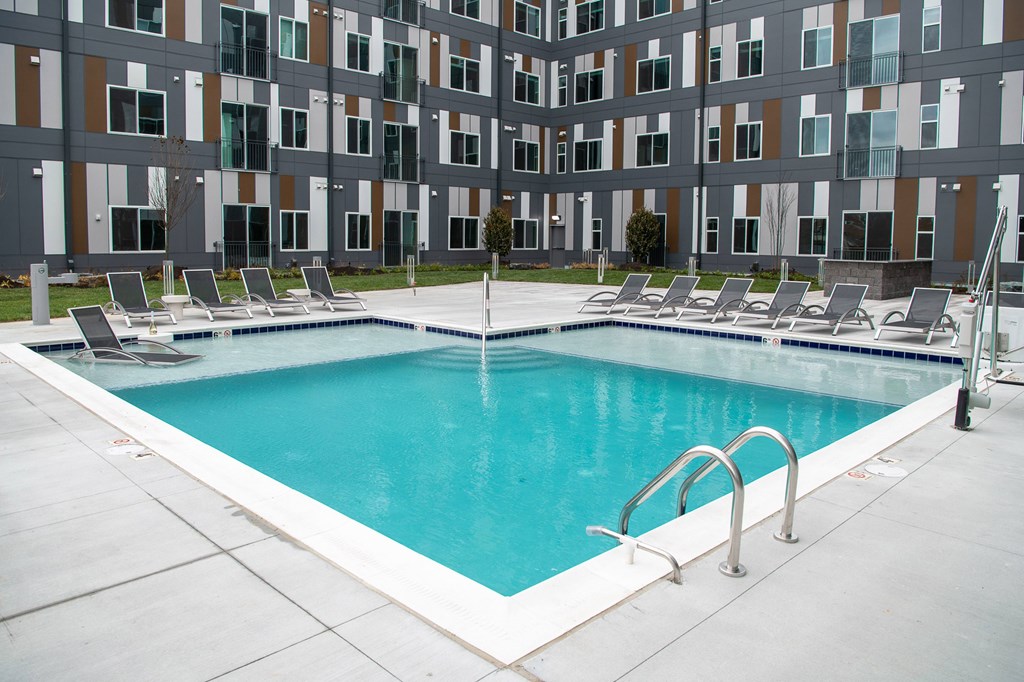 A large swimming pool in front of a building with lounge chairs around it.