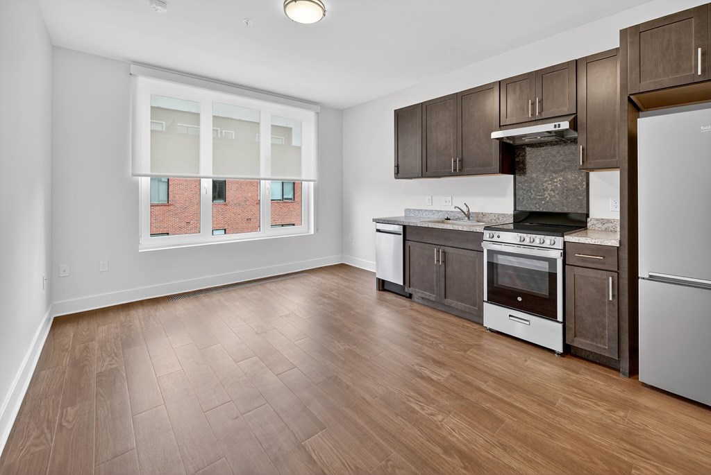 A kitchen with wooden floors and a window overlooking a brick building.