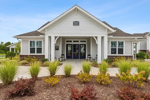 A white house with a black door and windows is surrounded by a garden.