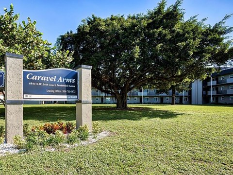 A sign for Caravel Arms in front of a tree and building.