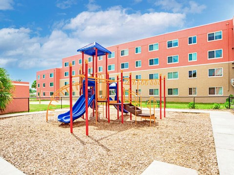 A playground with a blue slide and a red and yellow structure in front of a red building.