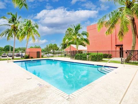 A swimming pool surrounded by palm trees and a red building.