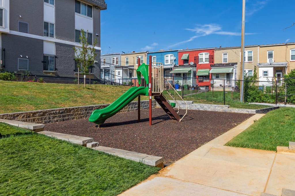 a playground with a green slide in front of an apartment building