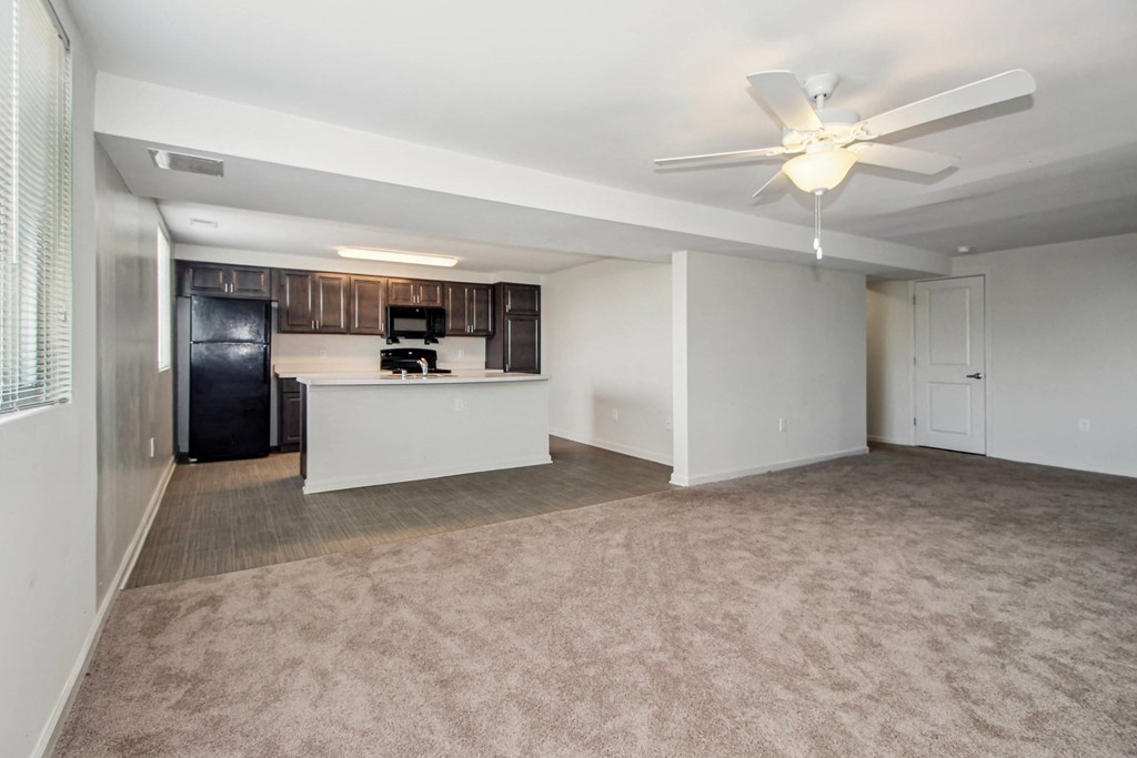 an empty living room with a kitchen and a ceiling fan