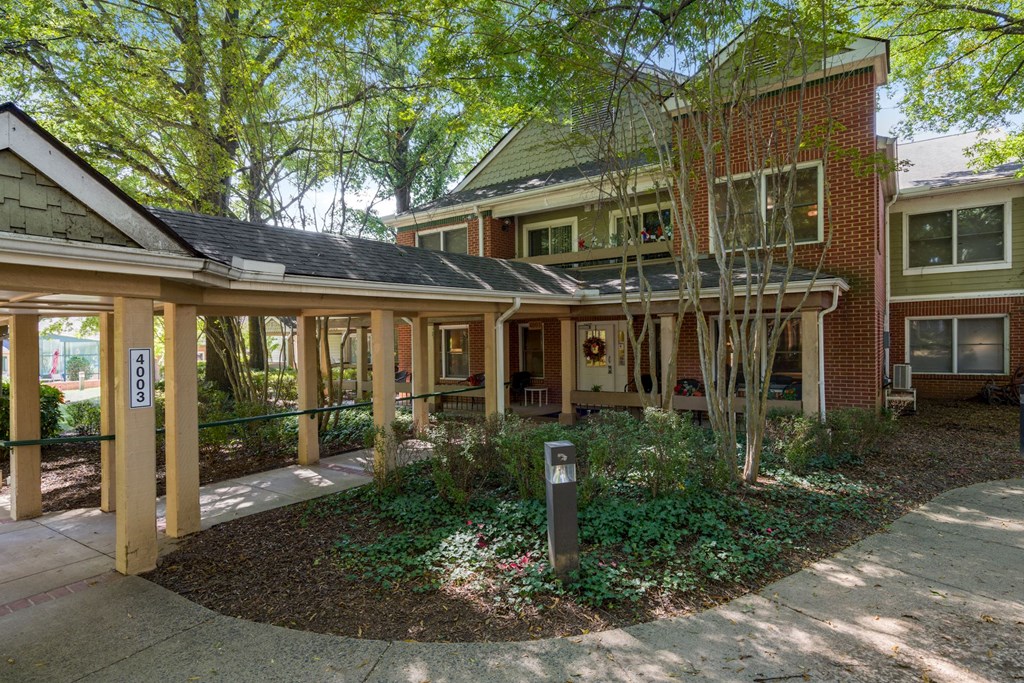 the front porch of a brick house with a sidewalk and trees