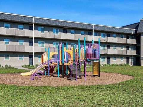 A playground with a slide, swings, and a monkey bars set in front of a building.