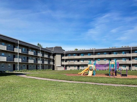 A playground with a slide and swings is in front of a large apartment building.