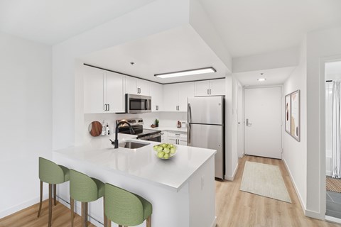 A kitchen with white cabinets and a white island with green chairs.