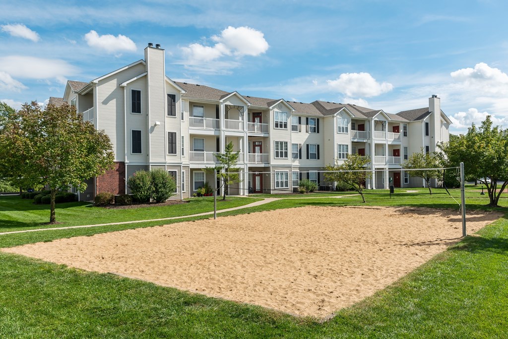 A large sandbox is in the foreground of a building with a green lawn.