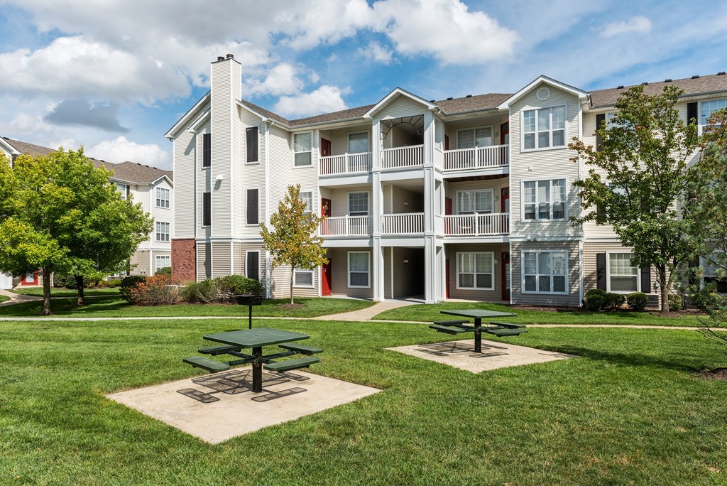 A large apartment complex with a green picnic table in the front yard.