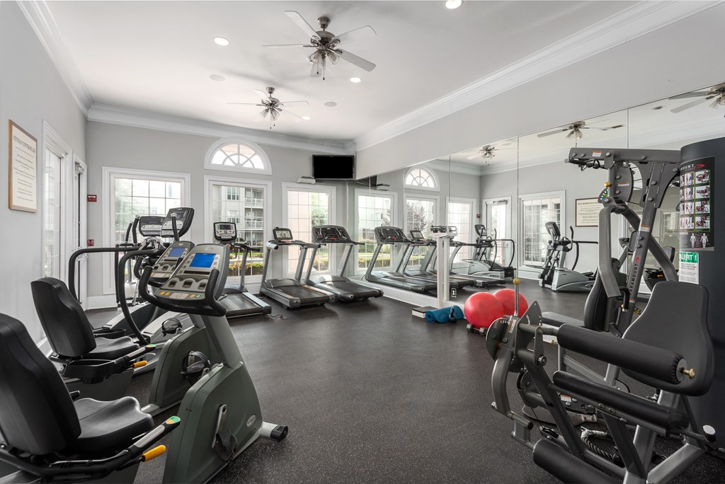 A spacious gym with various exercise machines and a ceiling fan.