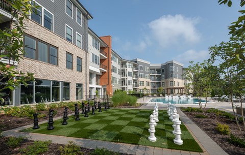 A chess set is set up on a lawn in front of apartment buildings.
