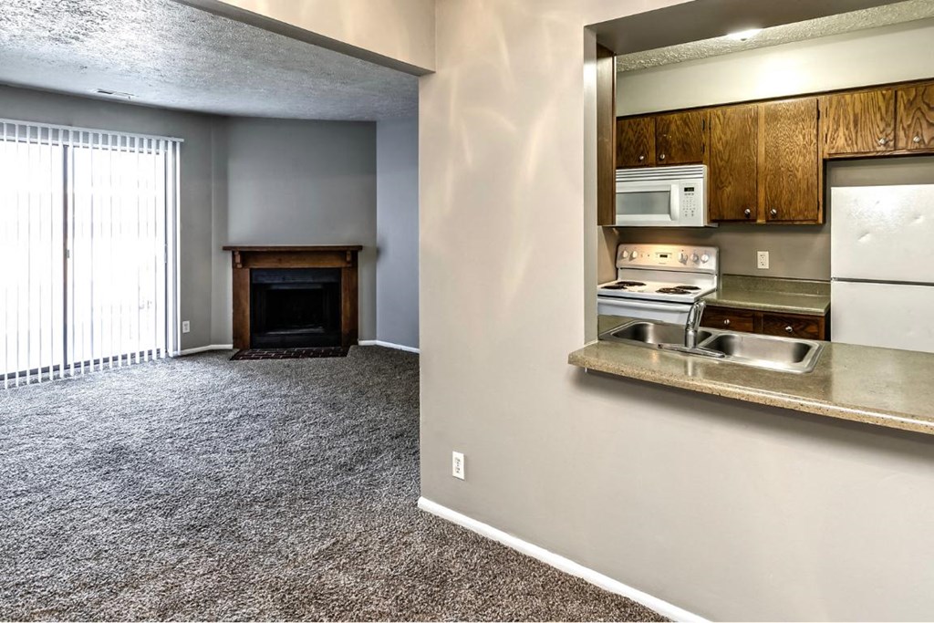 an empty living room with a kitchen with a stove and refrigerator