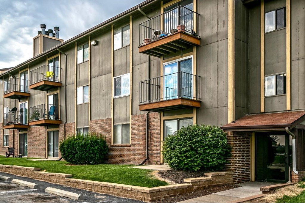 a brick apartment building with balconies and green grass