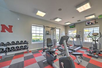 a gym with exercise equipment and windows at the at the village apartments