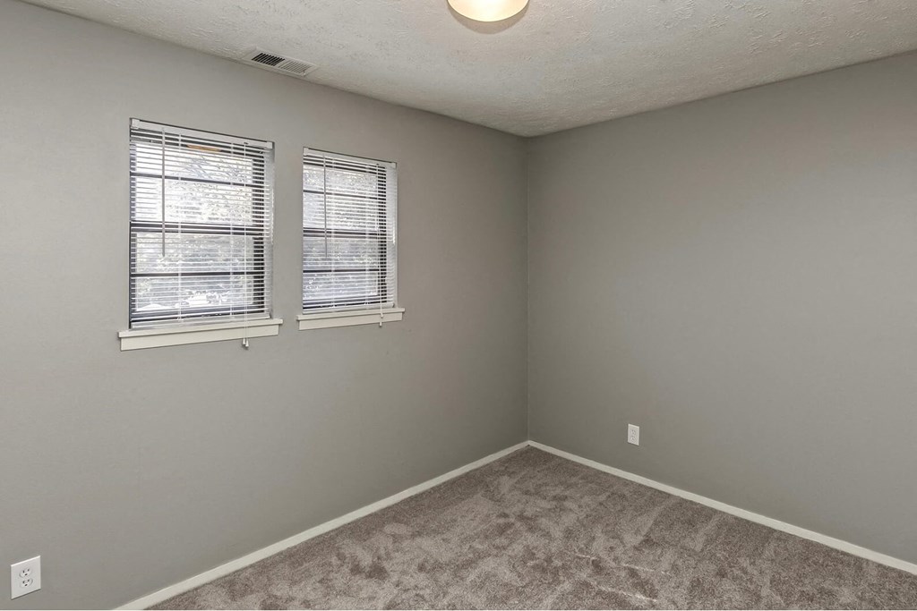an empty bedroom with two windows and a carpeted floor