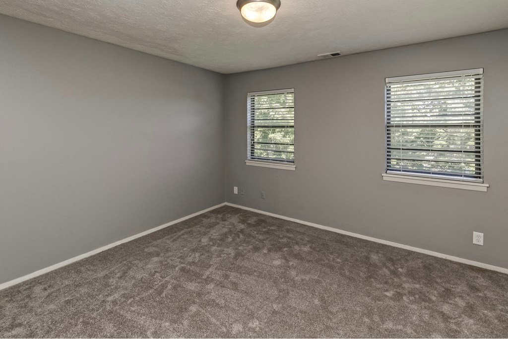 an empty bedroom with two windows and gray carpet