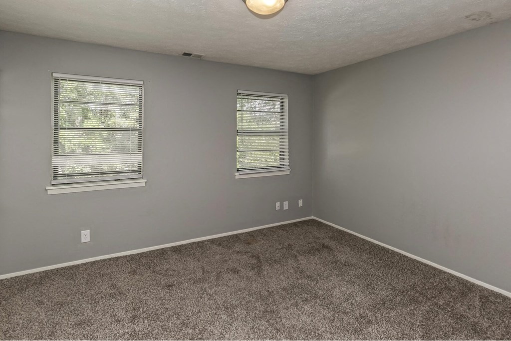 an empty room with carpet and two windows