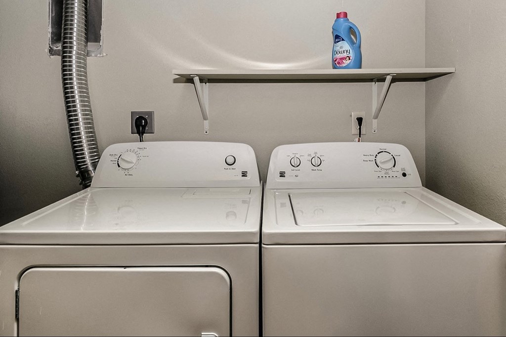 two washers and a dryer in a laundry room with a shelf above them